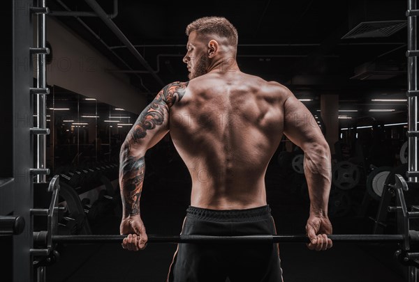 Portrait of an athlete sitting on a barbell in the gym. View from the back. Bodybuilding and fitness concept.