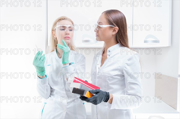Two beauticians pose in a medical office with cosmetic preparations and a syringe. Skin rejuvenation concept.