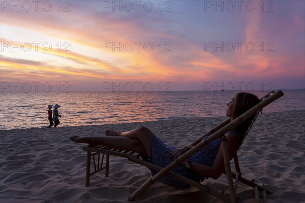 Woman lying in bamboo deckchair in evening mood on the beach