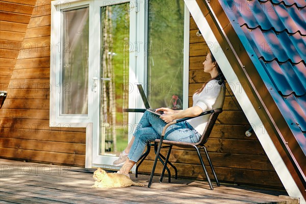 Digital nomad with laptop on veranda of tiny log house