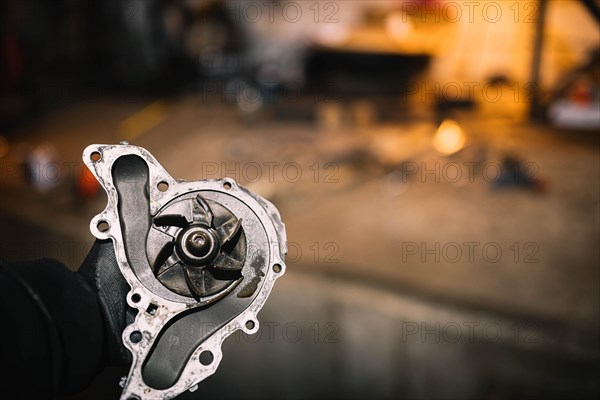 Automotive water pump of the engine cooling system in the hands of an auto mechanic