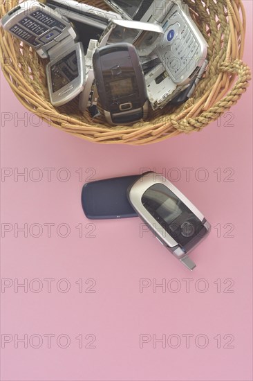 An assortment of vintage mobile phones in a basket with one flip phone placed in front