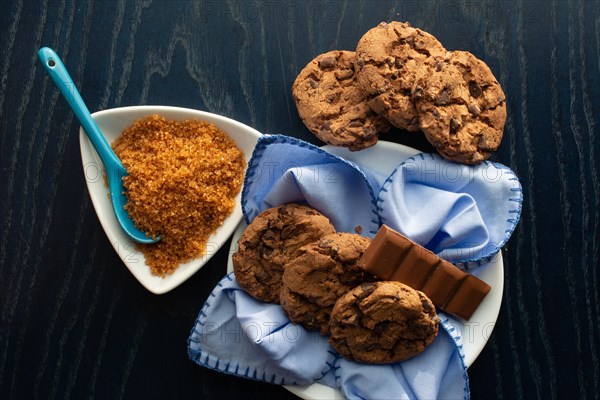 Chocolate chip cookies beside brown sugar and pieces of chocolate