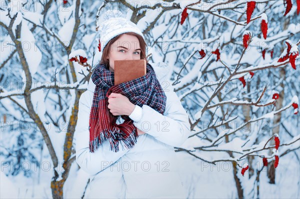 Portrait of a charming girl who reads a book in the winter forest. Concept of Christmas