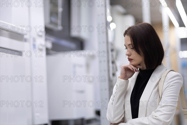 Beautiful young woman in a white jacket chooses plumbing supplies in a hardware store