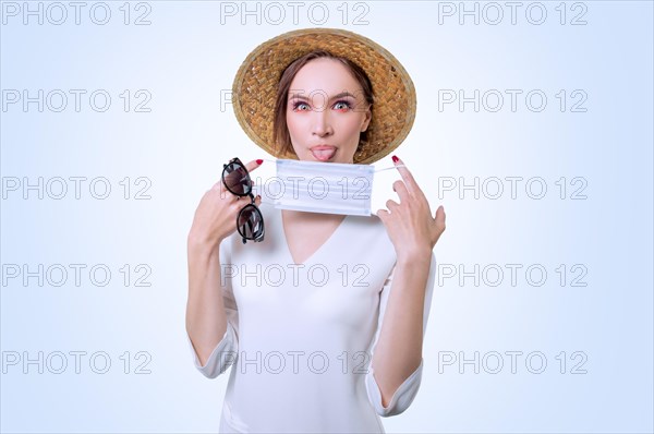 Beautiful girl posing on a white background in a yellow hat. She has a medical mask in her hands. The concept of tourism during the epidemic.