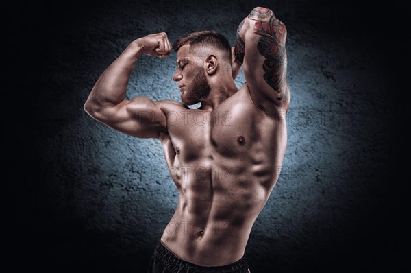 Young muscular guy with a nice abs posing against the backdrop of a blue spot. Fitness and nutrition concept.