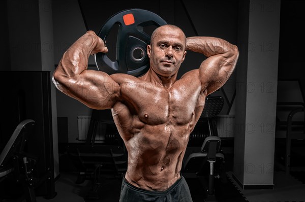 Muscular man posing in the gym with a barbell disc. Bodybuilding and powerlifting concept.