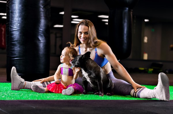 Charming sports mom trains in the gym with her little daughter and a French bulldog.