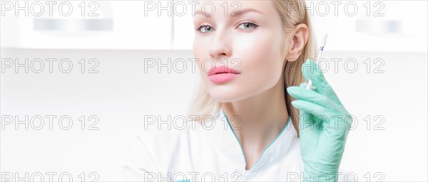 Portrait of a blonde girl in a medical gown with a syringe in her hands. Vaccination concept.