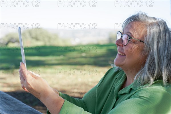Mature white-haired woman smiling looking at her digital tablet on a video call