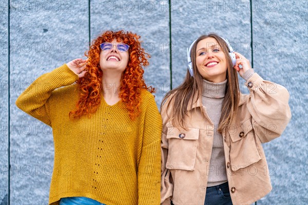 Frontal portrait of two happy women listening music with headphones standing in the city