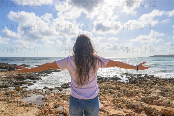 Middle-aged woman stretching her arms breathing fresh air on the Mediterranean coast in front of the sun