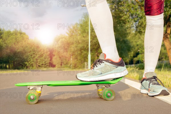 Images of a leg standing on a skateboard. Sunny evening in the park. Skateboarding concept.