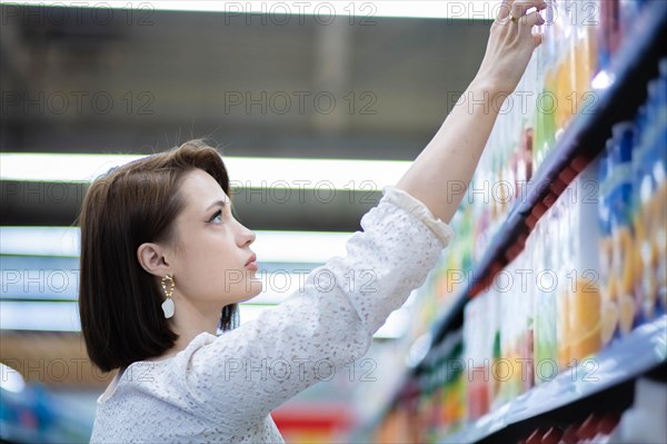 Beautiful young woman in a white dress chooses goods in a grocery store