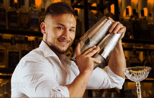 Charming bartender prepares cocktails in two shakers.