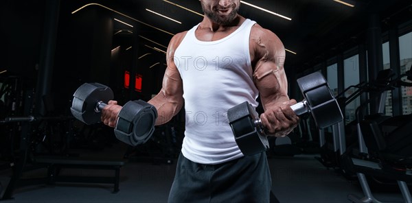 Portrait of a man in a white T-shirt exercising in the gym with dumbbells. Biceps pumping. Fitness and bodybuilding concept.