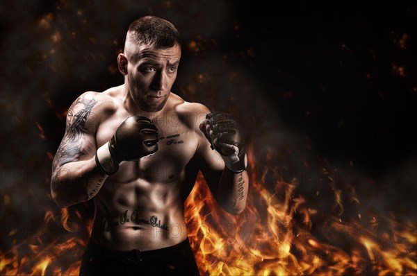 Mixed martial artist posing against the backdrop of fire and smoke. Concept of mma