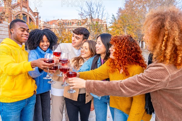 Diverse young people standing and toasting with red wine in the street