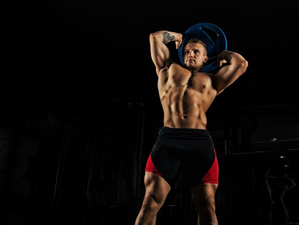 The weightlifter does the workout with burdening. He lifted a heavy pancake over his head and makes circular movements with his hips. Front view