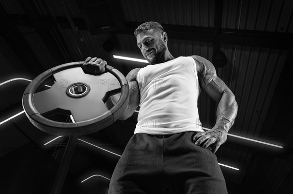 Portrait of a man in a white T-shirt exercising in the gym with barbell discs. Biceps pumping. Fitness and bodybuilding concept.