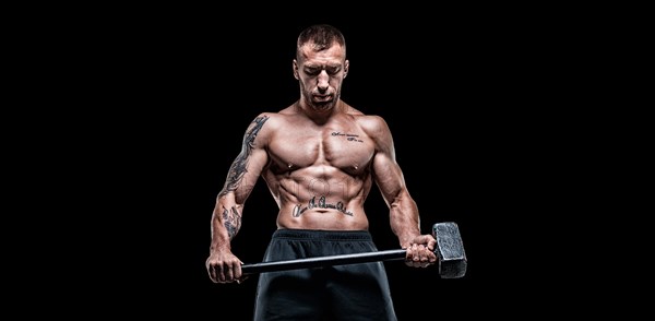 Professional sportsman stands with a sledgehammer in front of a rubber wheel. Functional training concept.