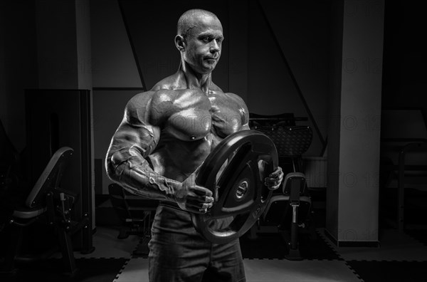 Muscular man posing in the gym with a barbell disc. Bodybuilding and powerlifting concept.