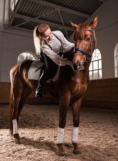 Image of a woman riding a thoroughbred horse. The background is a racing arena.