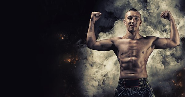 Portrait of a boxer of mixed martial arts standing against the backdrop of smoke and fire and celebrating a victory. The concept of sports