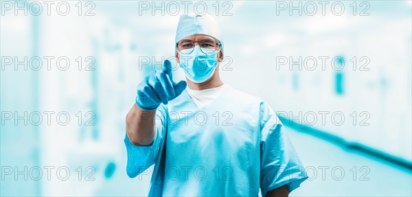 Portrait of a doctor in a hospital. He points a finger at the camera. Medicine concept.