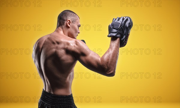 Muscular fighter posing with boxing paws in the studio on a yellow background. Mixed martial arts concept. High image quality