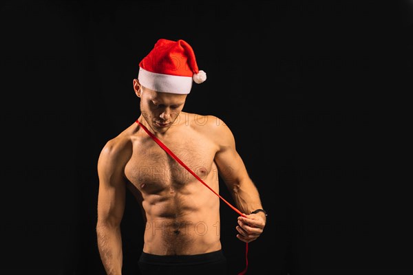 Sexy athletic man with a naked torso in a santa claus hat is preparing for a performance for christmas