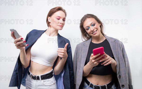 Two girlfriends are texting on their smartphones and laughing. Bloggers concept. Gossips.