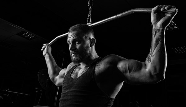 Professional athlete performs an exercise in the gym. Pulls the bar to the back of the head. Exercise for development of back muscles