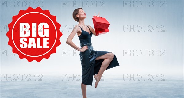 Beautiful tall girl enjoys shopping. She is holding red packages in her hands and showing the sign success .