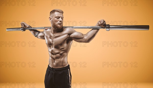 Young muscular guy posing with a barbell bar on his shoulders on an orange background. Fitness and nutrition concept.