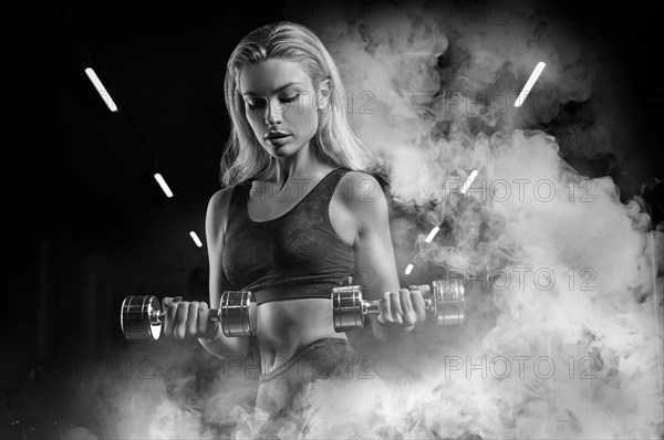 Charming sportswoman posing in the gym with dumbbells. The concept of bodybuilding