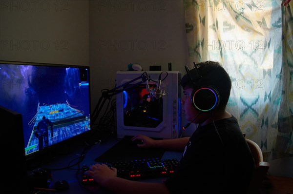 Side View of teenage gamer boy playing video games online on computer in dark room