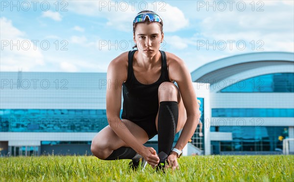 Portrait of a young runner who laces her boots at a football stadium. Sports concept.