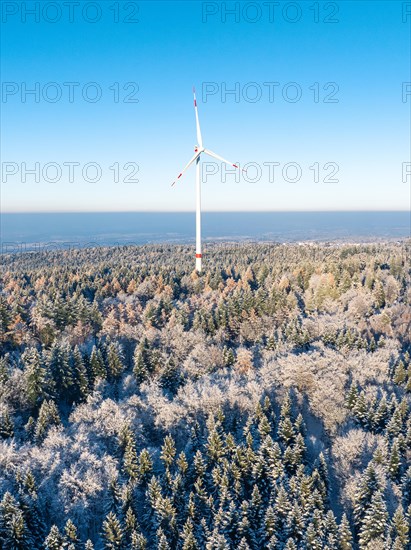 Lone wind turbine stands in the snowy winter forest under a clear blue sky