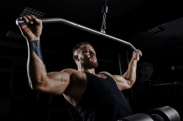 Professional athlete performs an exercise in the gym. Pulls the bar to his chest. Exercise for development of back muscles