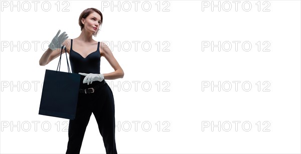 Beautiful young woman in white gloves holds a black craft bag in her hand. Shopaholics concept. Spenting. Gifts for the holidays. Black Friday. Shopping centers.