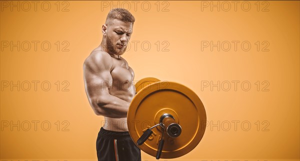 Young muscular guy pumps biceps with a barbell on an orange background. Fitness and nutrition concept.
