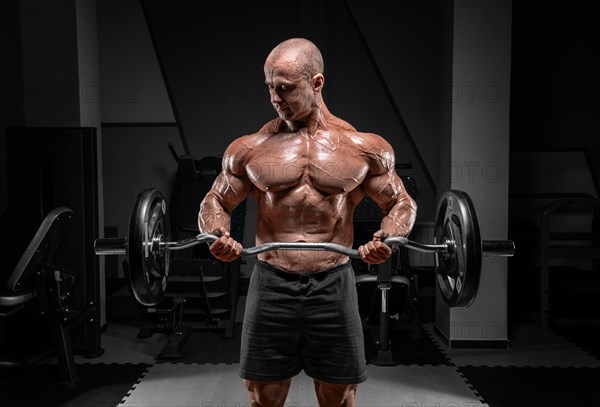 Professional weightlifter posing in the gym with a barbell in his hands. Classic bodybuilding.