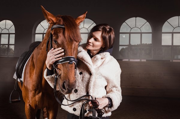 Portrait of a stylish woman hugging a thoroughbred horse. Love and care concept.