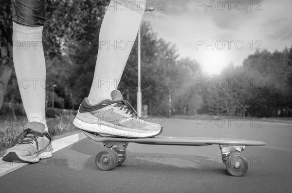 Images of a leg standing on a skateboard. Sunny evening in the park. Skateboarding concept.