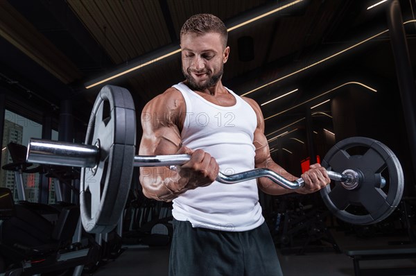 Handsome young man working out with a barbell in the gym. Biceps pumping. Fitness and bodybuilding concept.