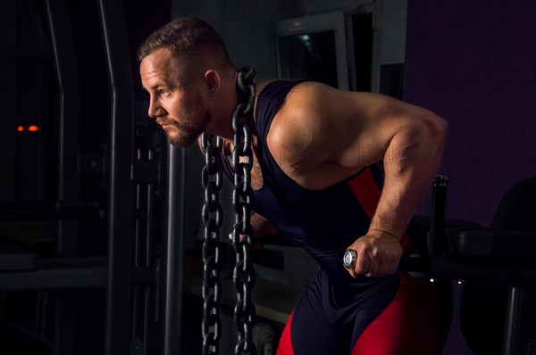 Weightlifter with a huge metal chain around his neck. Push-ups on the uneven bars in the gym