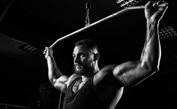 Professional athlete performs an exercise in the gym. Pulls the bar to the back of the head. Exercise for development of back muscles