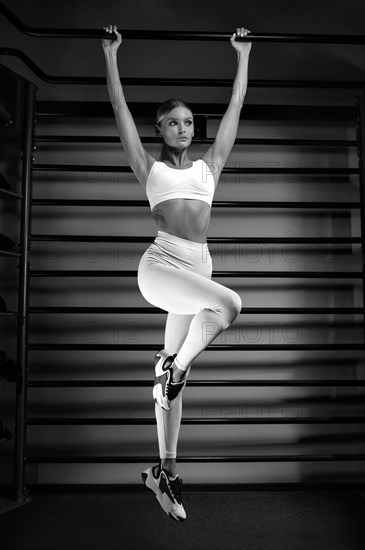 Beautiful tall blonde pulls up on the bar in the gym against the backdrop of the wall bars. The concept of sports